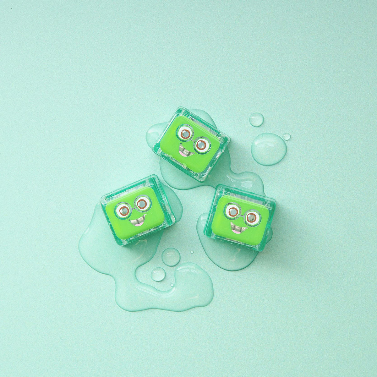 Three green Pippa Glo Pals light-up sensory cubes on a light blue surface with water droplets.