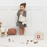 Little girl smiling while hugging a plush bunny and wearing a toy stethoscope near her vet kit.