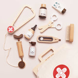 Flat lay of a wooden toy vet kit including a stethoscope, syringe, thermometer, scissors, brush, pet care medicine bottles, and a canvas medical bag.