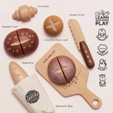 Wooden toy bakery play set featuring a cutting board, bread knife, croissant, and various toy loaves.