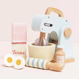 Wooden toy baking set including a pastel blue mixer, bowl, rolling pin, milk bottle, eggs, and ingredient boxes.
