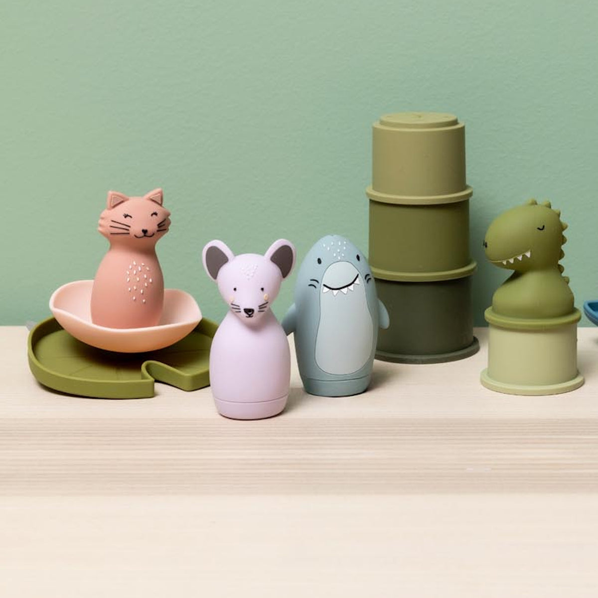 Colorful animal bath toys including a pink cat, purple mouse, blue shark, and green dinosaur on a shelf.