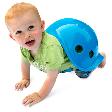 A young toddler crawls while wearing a blue Bilibo sensory toy on his back like a snail shell against a white background.