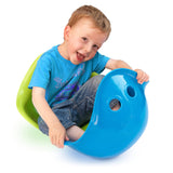 Smiling young boy playing with blue and green Bilibo sensory toys against a white background.