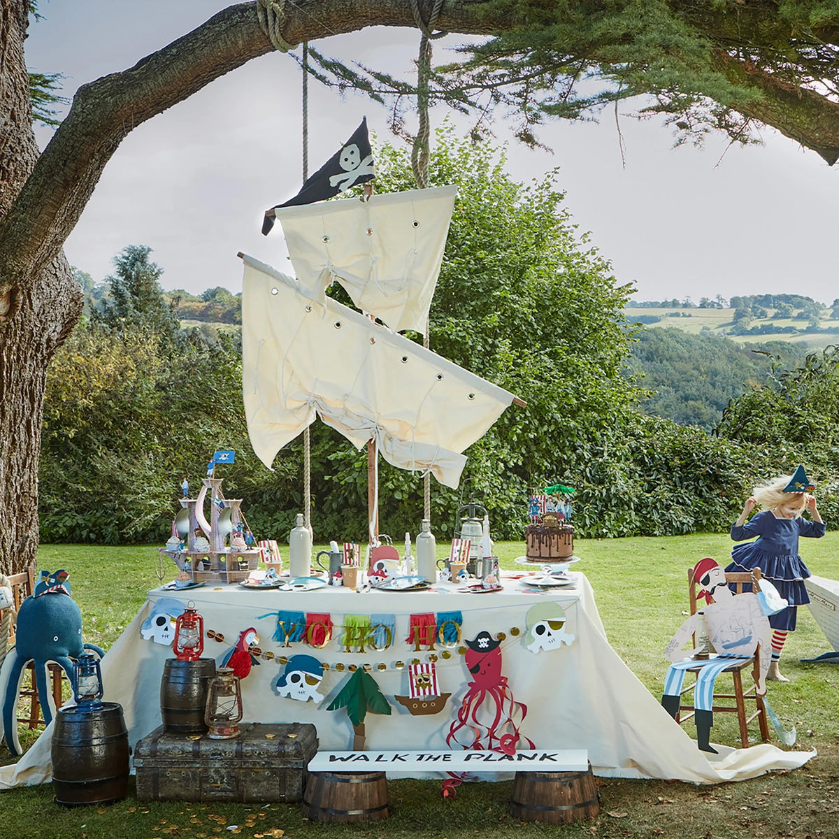 A pirate-themed outdoor party table with sails, flags, skulls, and a "Yo Ho Ho" banner in a grassy field.