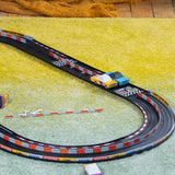 Candylab Roadworks toy cars racing on an oval track over a yellow rug. SEO-friendly wooden speedway playset lifestyle.