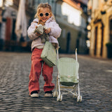 Toddler playing with a sage green Dinkum Dolls convertible changing bag and matching toy stroller.