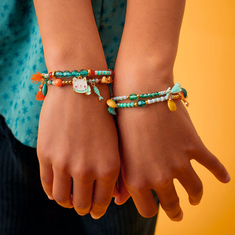 Girl wearing stacked Hanae cat collection beaded charm bracelets with enamel cat fish and tassel pendants.