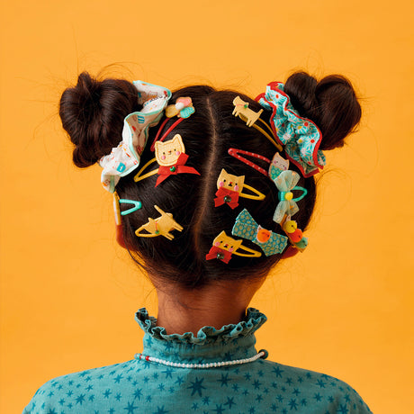 Girl wearing colorful cat themed hair clips and scrunchies in double buns against a bright yellow backdrop