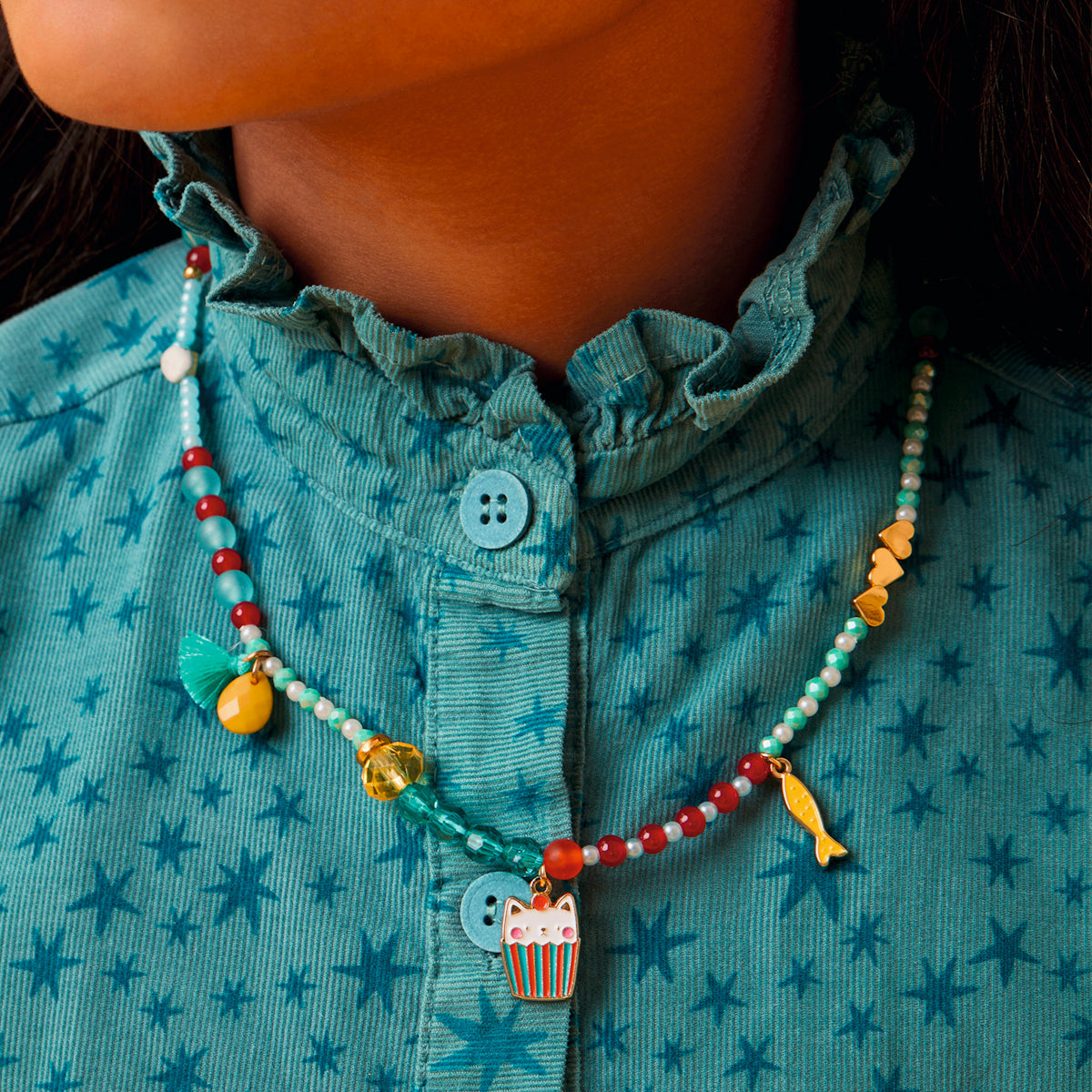 Girl wearing Mia cat collection beaded necklace with enamel cat cupcake and fish charms in teal and red.