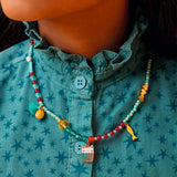 Girl wearing Mia cat collection beaded necklace with enamel cat cupcake and fish charms in teal and red.