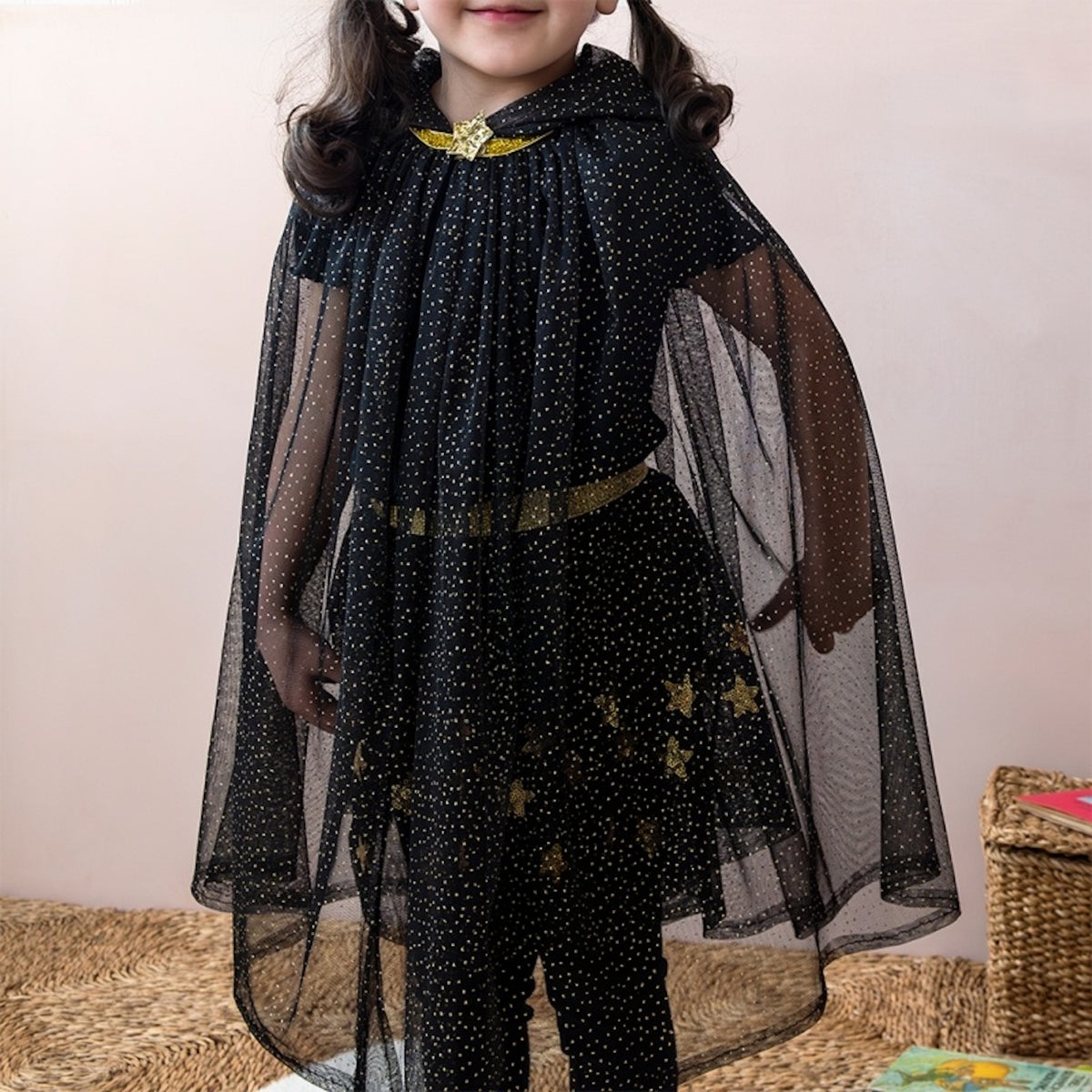Young child wearing a sheer black dress-up cape sprinkled with gold glitter dots and fastened with a gold star closure.