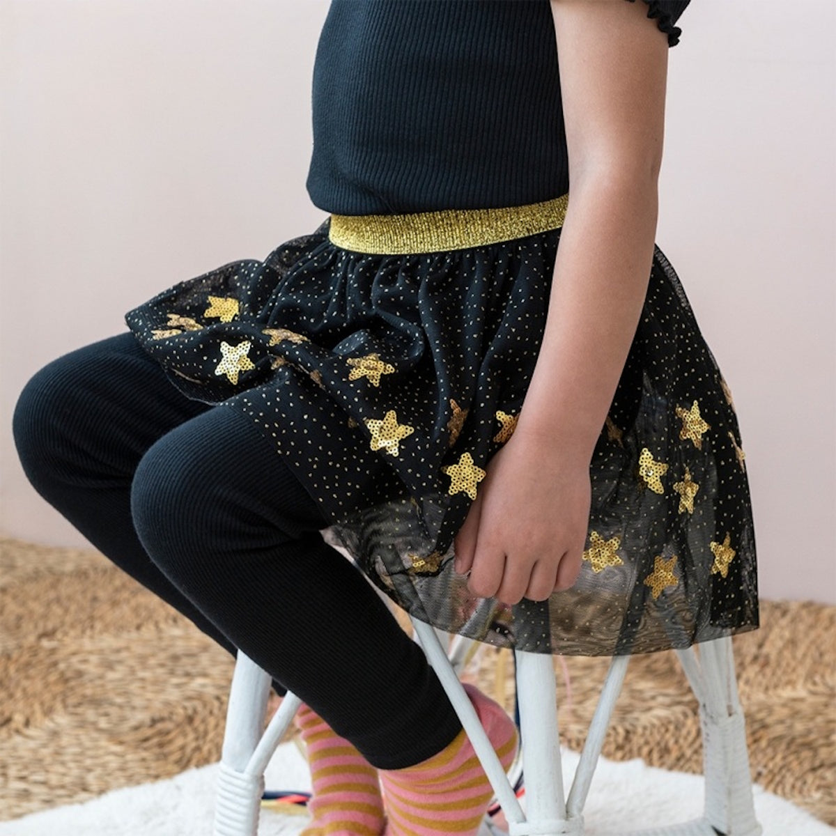 Child sitting down, wearing a black tulle dress-up skirt with gold sequin stars and black leggings.