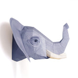 A paper sculpture of an elephant's head with a raised trunk, featuring geometric patterns and textures, set against a plain white background.