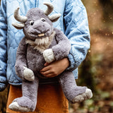 A person in a blue jacket holding a plush grey horned creature toy outdoors.
