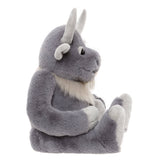 Side profile of a plush grey horned creature toy sitting down, showing curved horns and light fur beard.