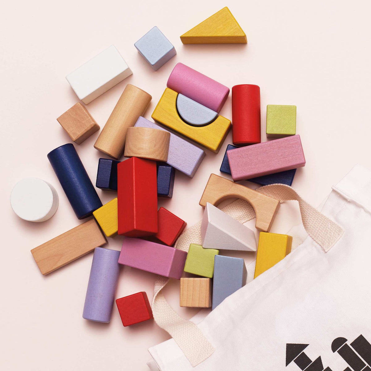 Assorted colorful wooden building blocks overflowing from a white fabric storage bag.