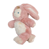 Side view of a plush baby doll in a fuzzy pink bunny suit with floppy ears and a rainbow emblem.