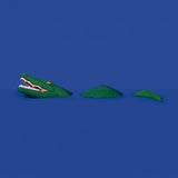 A 3D papercraft crocodile made of green segments appearing to swim across a solid blue background.