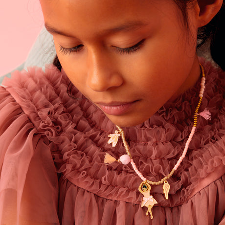 Girl wearing a dance collection beaded necklace with ballerina and ballet shoes charms in pink gold.
