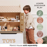 Young boy looking inside a wooden dollhouse filled with miniature furniture.