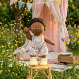 Olli Ella Dinkum Doll in a floral Suki dress standing on a stool outdoors.