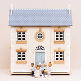 Seven wooden family figures gathered in front of a beige dollhouse with a blue door and roof.