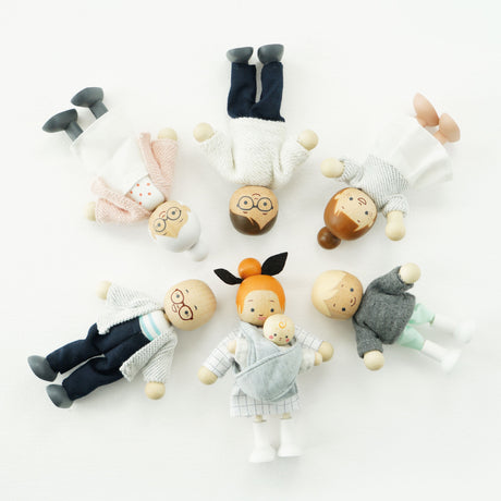 Seven wooden dollhouse family figures lying in a circle with heads pointing toward the center.