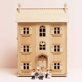 Seven wooden family figures and a dog toy standing in front of a three-story wooden dollhouse.