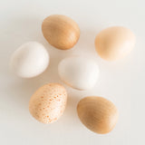 Toy wooden eggs in assorted finishes arranged on a white surface.