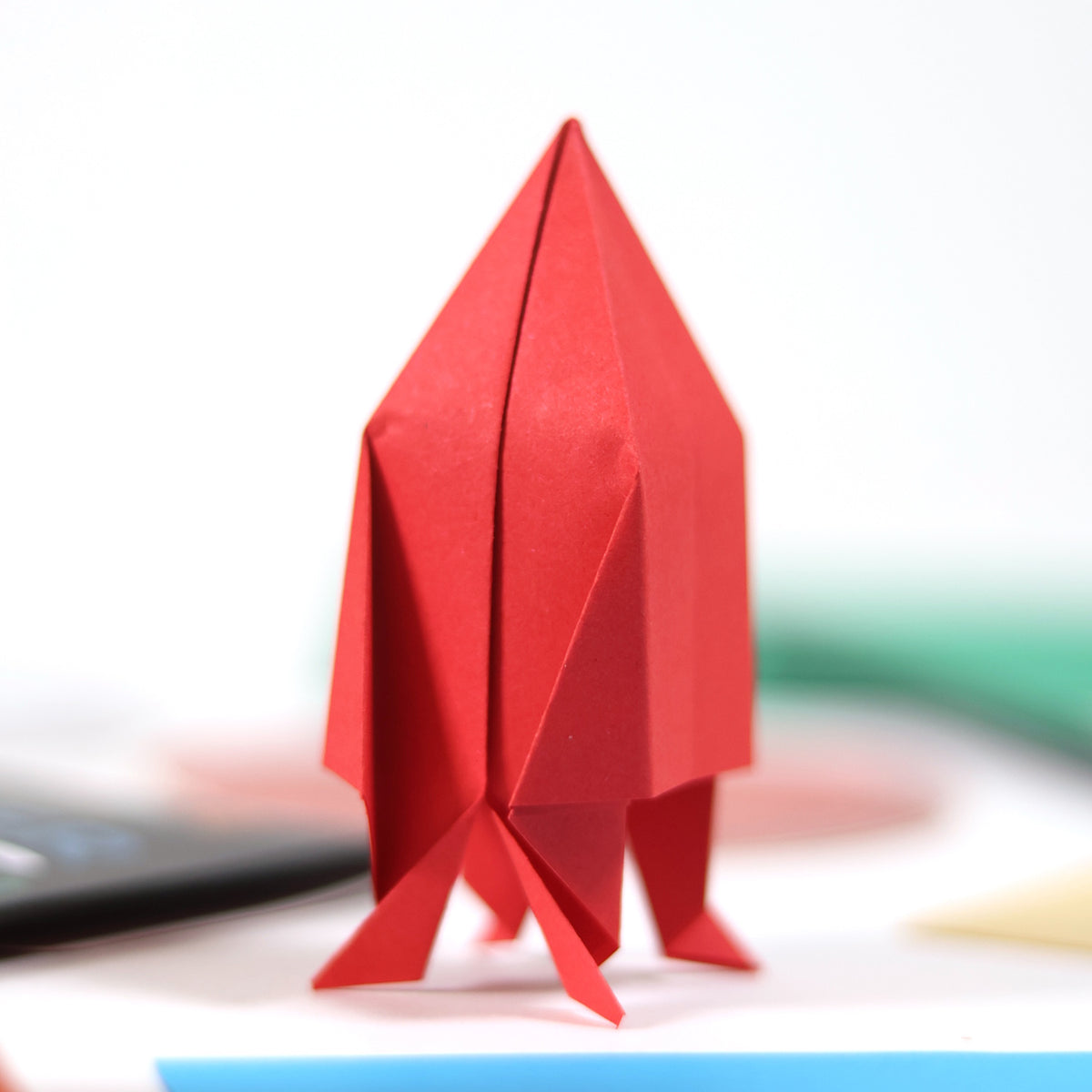 Red origami paper rocket standing upright on a white surface.