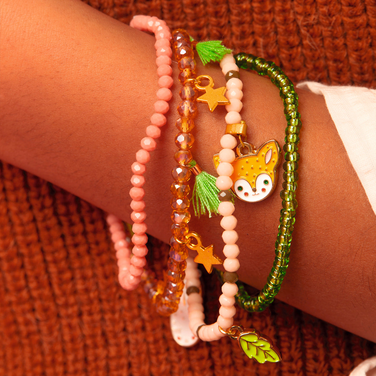 Girl wearing stacked Automne forest collection bracelets with enamel deer and leaf charms in pink and green.