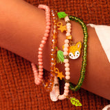 Girl wearing stacked Automne forest collection bracelets with enamel deer and leaf charms in pink and green.
