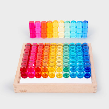 Colorful transparent counters in red, orange, yellow, green, and blue, arranged neatly on a mirrored wooden tray and scattered around it, creating a playful and vibrant tone.