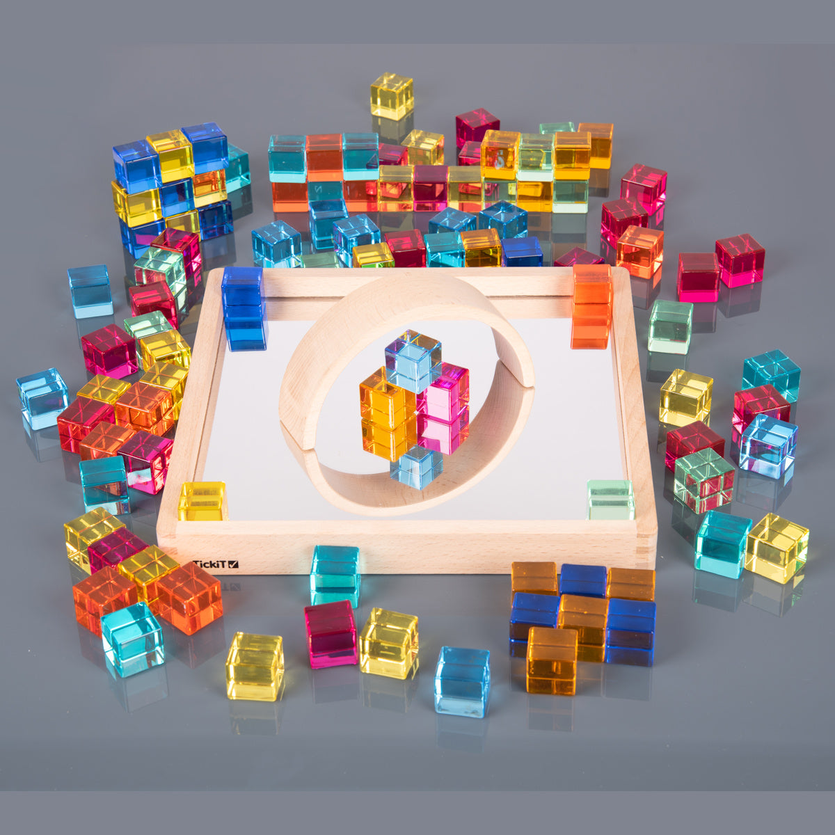 A square wooden tray with a mirrored base and colorful gem-like insets, designed to inspire sensory exploration, pattern making, and visual play.