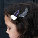 Close-up of a child wearing a glitter ghost and a black bat hair clip side by side.