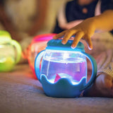 Child tapping the lid of a glowing blue Glo Pals Mini Sensory Play Jar filled with water.
