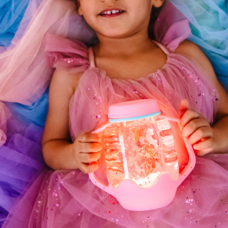 Child in a pink dress holding a glowing light-up sensory jar with handles.