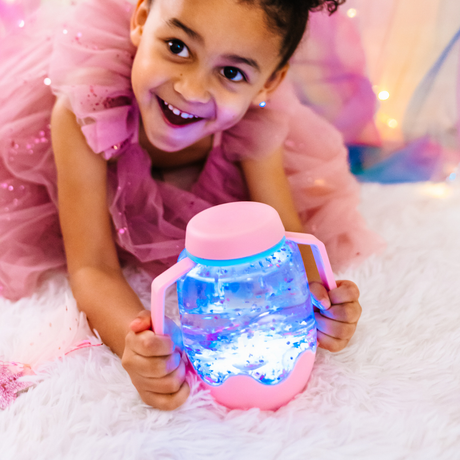 Smiling girl lying down while holding a pink glowing light-up sensory jar.