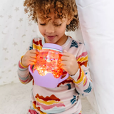 Child holding and looking down at a glowing orange-lit Glo Pals sensory play jar with a purple base.