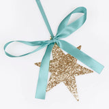 Close-up of a gold glitter star ornament tied with a mint green satin ribbon tied into a bow.