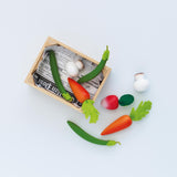 Wooden play vegetables with felt tops arranged beside and inside a newspaper-lined crate.