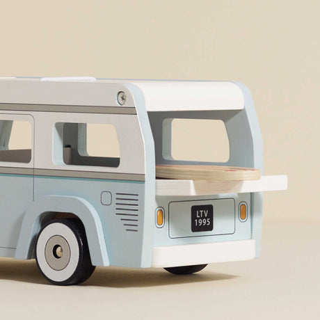 Wooden toy camper van in light blue and white with a surfboard sticking out of the open back.