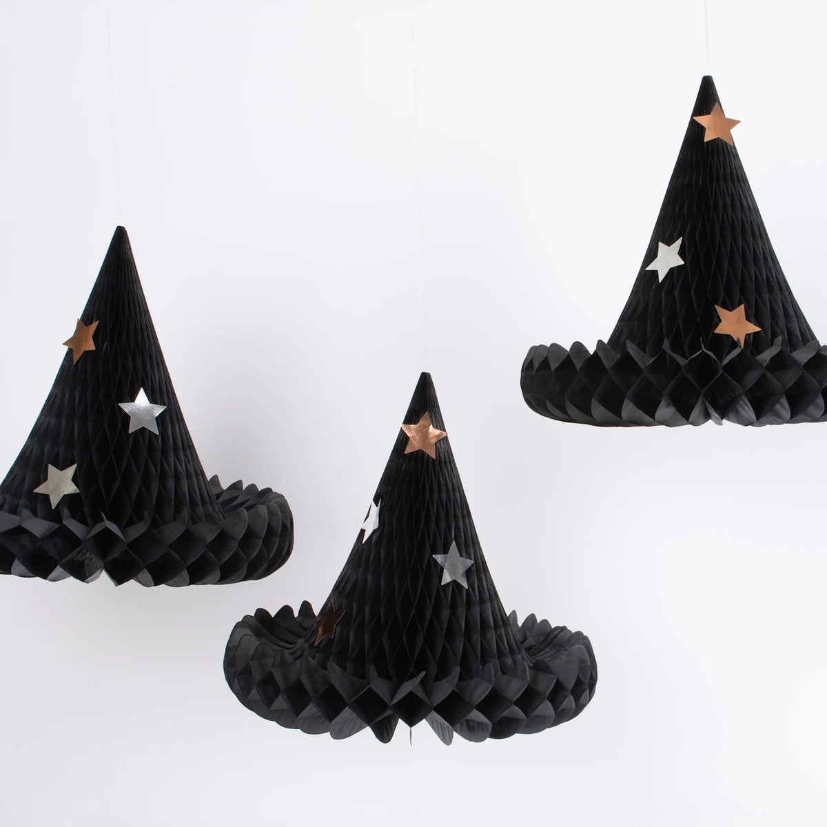 Three black honeycomb paper witch hat decorations adorned with metallic star accents hanging against a white backdrop.