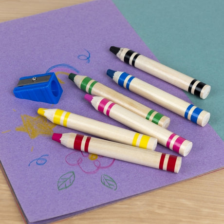 Six jumbo wooden crayons and a blue sharpener on purple paper with child drawings.