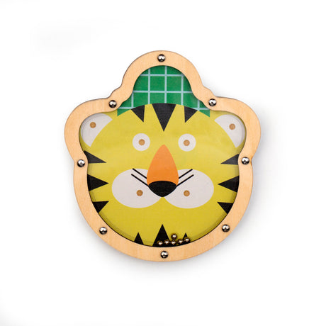 Wooden puzzle depicting a smiling cartoon tiger face with a yellow background and green grid pattern. Small metal balls are inside. Playful tone.