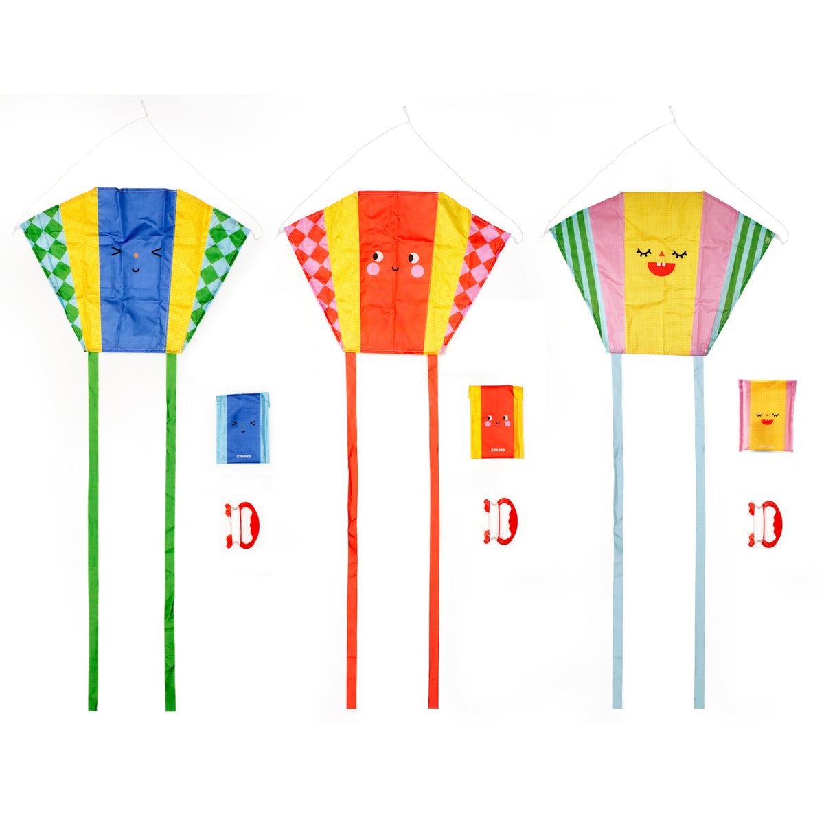 Three colorful kites with smiling faces and long tails. Each kite has a matching carrying pouch and a red handle below them. Playful and cheerful vibe.