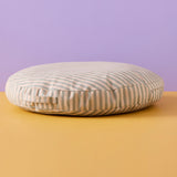Round sage green and beige striped floor cushion with a fabric handle against a two-tone background.