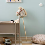 Striped fabric hobby horse leaning against a wooden crib in a decorated playroom.