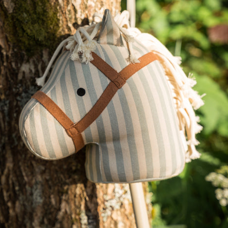 Close-up of a striped fabric hobby horse head leaning against a tree outdoors.
